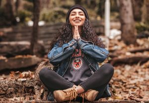 A girl sitting cross legged, with her hands in a prayer position and smiling